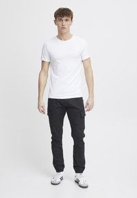 Hvid kortærmet t-shirt med rund hals, parret med sorte cargo-bukser. Sneakers har en hvid overdel med grå og blå accenter.