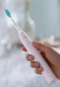 Spazzolino elettrico Sonicare, con un manico rosa, una testina bianca con setole verdi e un pulsante di accensione con una spia verde.
