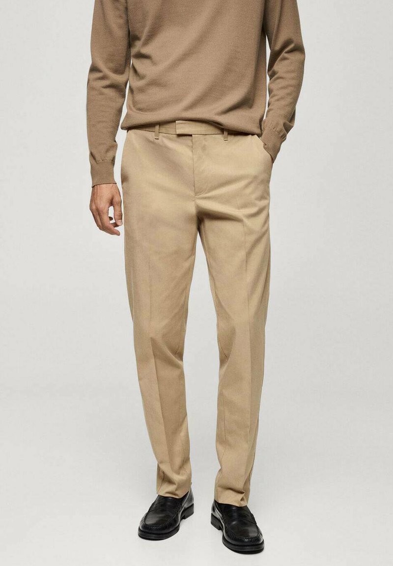 Pantaloni beige in tessuto liscio, con un design a gamba dritta e passanti per la cintura. Abbinati a scarpe nere.