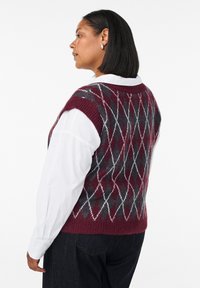 Burgundy a šedý károvaný svetr s žebrovaným výstřihem; nošený přes bílou košili s knoflíčky, zobrazený z boku s vodorovným lemem.