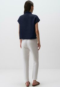 Top in lino blu navy con maniche corte e colletto alto, abbinato a pantaloni in lino bianchi. L'outfit presenta una vestibilità comoda e un design minimale.