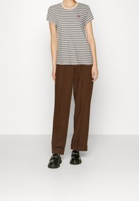 Striped grey and white t-shirt with a round neckline and a small logo, paired with brown wide-leg pants and black chunky shoes.