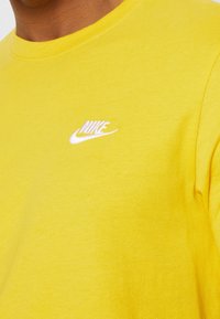 Yellow cotton T-shirt with a rounded neck, featuring a small white Nike logo on the chest. Smooth texture, casual design.