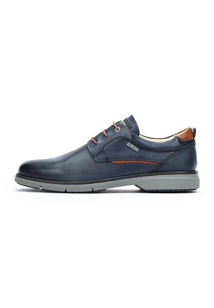 Zapato de cuero navy con un acabado suave, suela de goma gris, acentos de cuero marrón y cordones beige. Presenta un diseño clásico con detalles laterales.