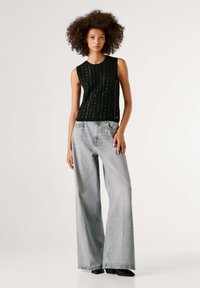 Μαύρο πλεκτό αμάνικο τοπ με κάθετα σχέδια, συνδυασμένο με ανοιχτό γκρι τζιν παντελόνι με φαρδιά τρέσα, που διαθέτει άνετη εφαρμογή και μινιμαλιστικό σχέδιο.