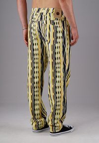 Lightweight patterned pants featuring yellow and black vertical stripes, with a relaxed fit and back pockets. Fabric has a soft texture.