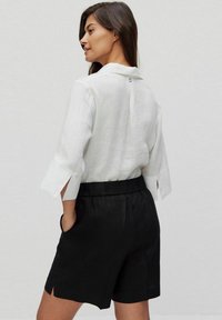 Vit linneskjorta med krage och breda, uppvikt ärmar, kombinerad med svarta linneshorts med elastisk midja och sidofickor.