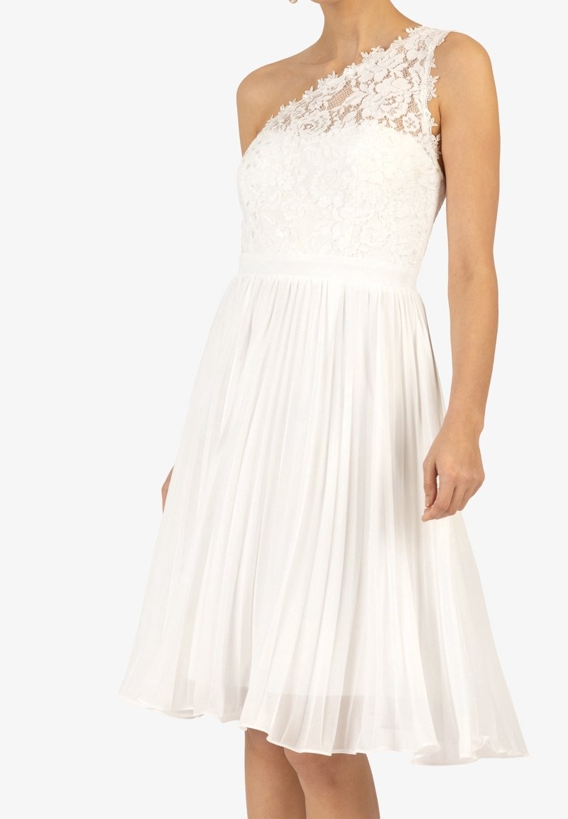 Bílé šaty s jedním krajkovým ramínkem, plisovanou sukní, přiléhavým korzetem a texturovanými květinovými krajkovými detaily. Hladká, lehká tkanina.