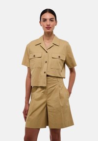 Chemise kaki courte à manches courtes avec deux poches poitrine, associée à un short taille haute à plis. Le tissu semble léger et doux.