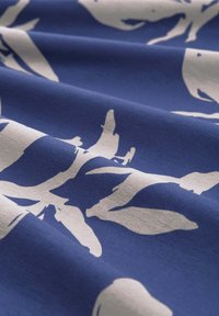 Kangas katun yang memiliki latar belakang biru dengan siluet kehidupan laut berwarna putih. Teksturnya halus dengan lipatan lembut yang menonjolkan desain.