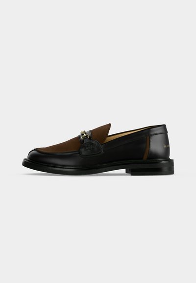 Μαύρο δερμάτινο loafers με καφέ σουέντ επάνω μέρος, λεπτομέρεια από χρυσό μεταλλικό κομμάτι και χαμηλό στοίβαγμα τακουνιού σε απλό λευκό φόντο.