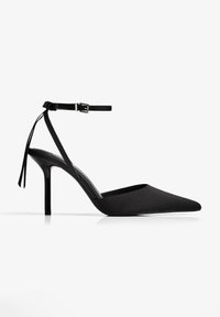 Fekete, hegyes orrú magassarkú cipő, sima anyagból készült, bokapánttal, kis csattal és két anyagbojt simítással.