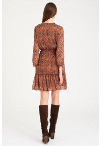 Pitkähihainen, paisley-kuvioinen mekko maanläheisissä sävyissä, jossa on röyhelöhelma. Varustettu vyötärölle sidottavalla nauhalla ja yhdistetty pitkien ruskeiden mokkabootsien kanssa.