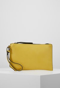 Geel rechthoekige armbandclutch met een zwarte rits en een smalle polsband op een wit oppervlak tegen een effen achtergrond.