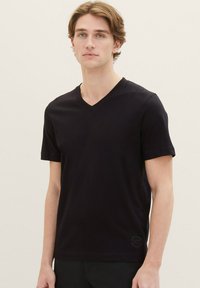 Zwarte T-shirt met korte mouwen en V-hals, gemaakt van zacht stof, met een subtiele textuur en een rond logo op de rechteronderzoom.