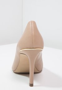 Chaussure à talon haut beige avec un embout pointu, finition en cuir lisse et un talon stiletto fin. Présente un accent doré subtil à la semelle.