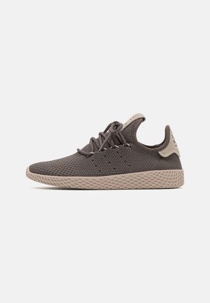 Lavskåret mørkegrå strikket sneaker med beige struktureret sål og snørebånd, sidevisning på en ensfarvet lys baggrund.