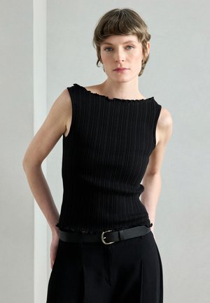 Sort ribstrikket tanktop med bølget halsudskæring og tætsiddende pasform. Kombineret med sorte bukser med høj talje og et slankt bælte med en rund spænde.