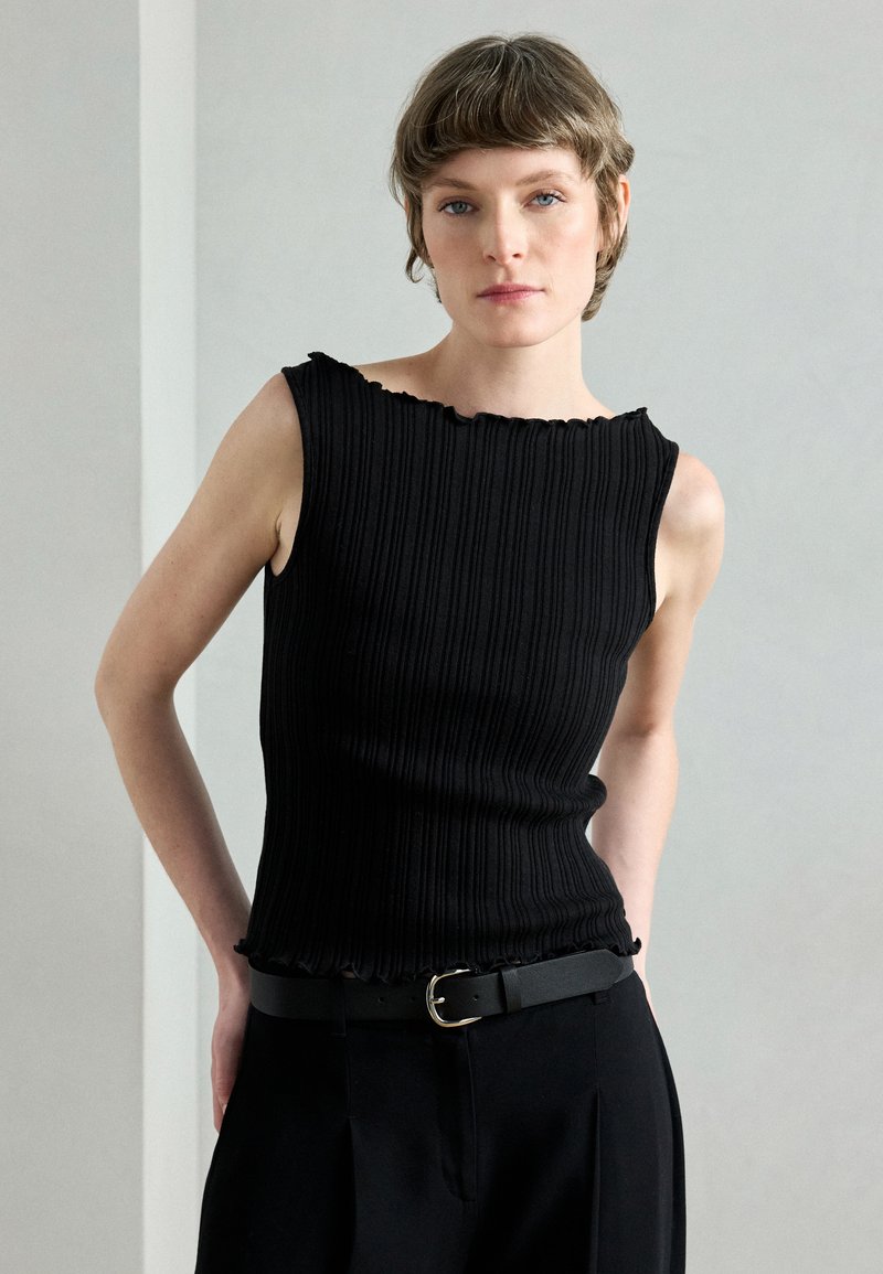 Μαύρο ριμπ τοπ με κυματιστό λαιμόκοψη και εφαρμοστή σχεδίαση. Συνδυάζεται με ψηλόμεσο μαύρο παντελόνι και λεπτή ζώνη με στρογγυλό αγκράφα.