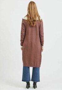 Lång, mauve kardiagan med ribbad nederkant och manschetter, med en vit spetskrage. Buren över blå utsvängda jeans och svarta klackstövlar.