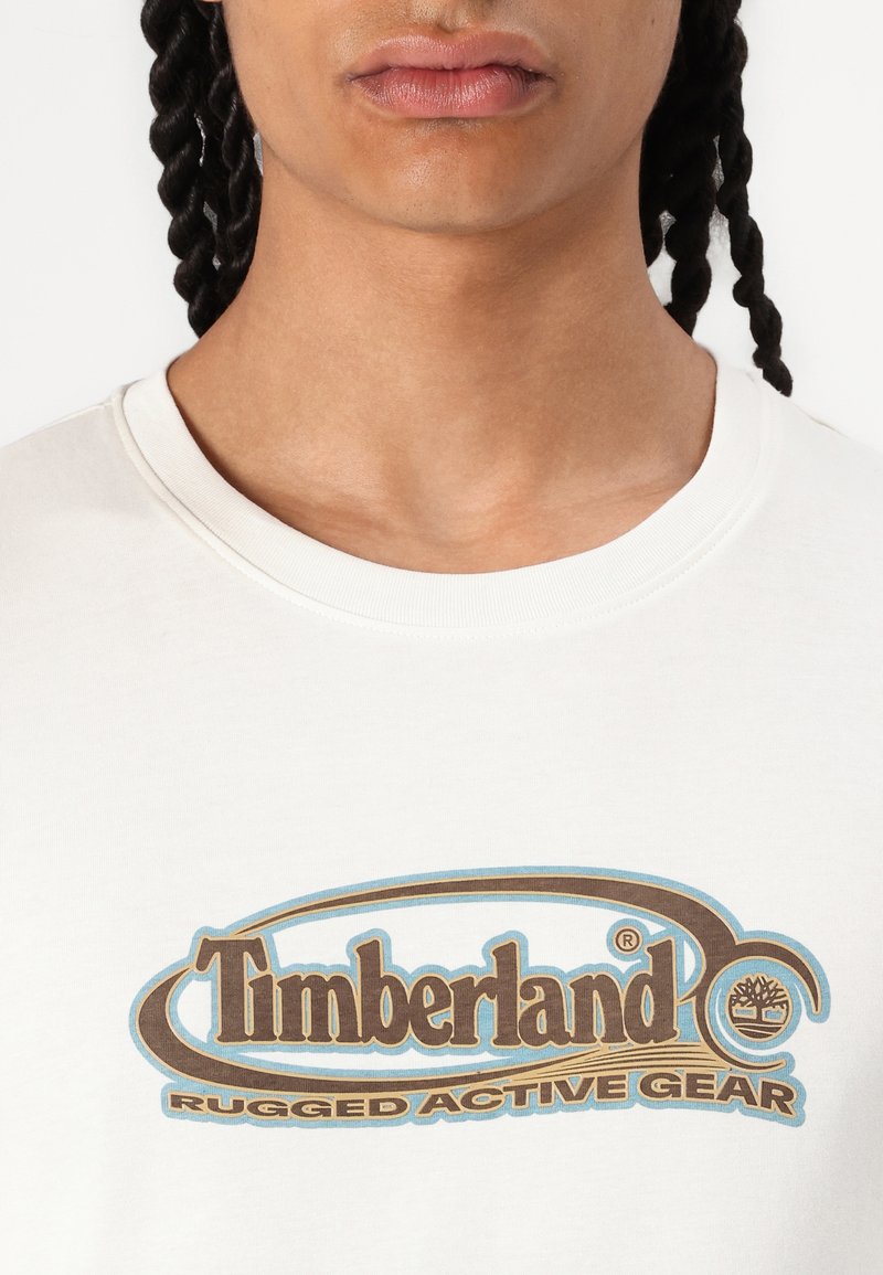 Witte katoenen t-shirt met een ronde bruine en blauwe "Timberland Rugged Active Gear" logo op de borst en een ronde hals.