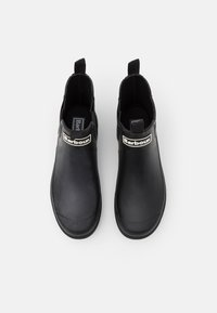 Bottes de cheville en caoutchouc noir avec une surface lisse, un bout arrondi et un patch logo contrastant sur le devant. Panneaux latéraux élastiques pour un enfilage facile.