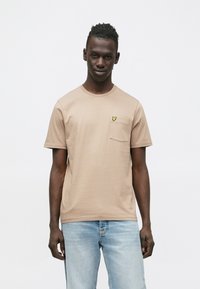 Tankleurig T-shirt met korte mouwen en ronde hals, voorzien van een zakje en een klein geel vlindertje op de linkerborst. Gladde stoffenstructuur.