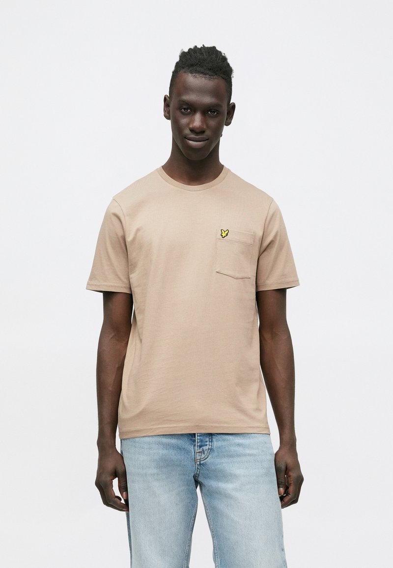 Tankleurig T-shirt met korte mouwen en ronde hals, voorzien van een zakje en een klein geel vlindertje op de linkerborst. Gladde stoffenstructuur.