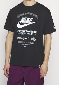 Černé bavlněné tričko s krátkým rukávem, zdobené vícebarevným logem Nike a grafickými texty. Uvolněný střih s etiketou na spodní levé straně.