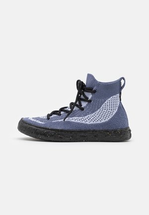 Basket montante avec empeigne en tissu tricoté violet et gris clair, lacets noirs et semelle en caoutchouc noire tachetée sur fond blanc.