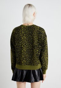 Sweatshirt verde e nero con stampa leopardata, collo rotondo e orlo a coste, con maniche lunghe e vestibilità comoda. Indossato sopra una gonna nera plissettata.