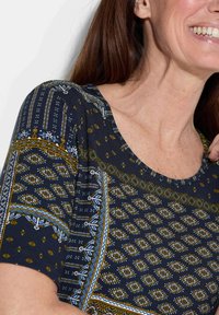 Korte mouwen top in marineblauw met geometrische patronen in goud en blauw. Heeft een ronde halslijn en een zachte stofstructuur.