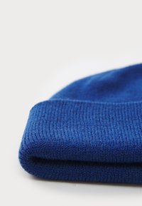 Blå strikket lue med brettet oppkant, som har et teksturert mønster og jevn overflate. Laget av mykt, fleksibelt materiale.