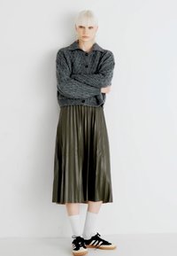 Cardigan cinza tricotado com colarinho, fechamento com botão; saia midi pregueada verde-oliva; ténis pretos com meias brancas; fundo simples.