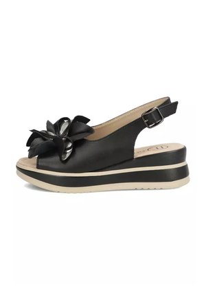 Czarna sandałka na koturnie z regulowanym paskiem wokół kostki, otwartym palcem i dekoracyjnym wielowarstwowym kwiatem z przodu, beżowa podeszwa z czarnym paskiem.