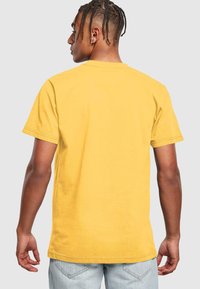 Gul bomulds T-shirt med korte ærmer, lige snit og en let struktureret overflade. Bagfra ses en ren halsåbning og kant.