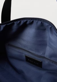 Εσωτερικό τσάντας ώμου από ναυτικό ύφασμα με ομαλή υφή, που διαθέτει μια τσέπη με φερμουάρ και μια μαύρη ετικέτα. Απλός, λειτουργικός σχεδιασμός.