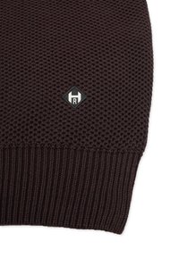 Braune Strickmütze mit strukturiertem Muster, geripptem Bund und einem kleinen schwarzen Diamant-Patch mit weißem Logo. Weiches und dehnbares Material.