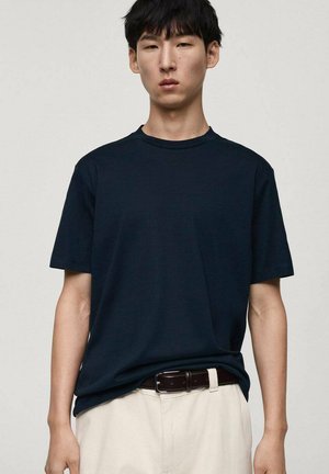 Marineblauwe katoenen T-shirt met een ronde hals en korte mouwen, gedragen boven off-white broek met een bruine riem. Gladde textuur, casual pasvorm.