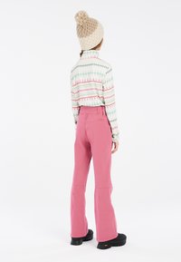 Haut à manches longues multicolores avec des motifs géométriques ; pantalon évasé taille haute rose ; bonnet en maille texturée beige ; chaussures noires.