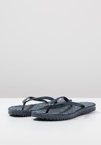 Infradito blu scuro con footbed testurizzato, cinturini lucidi e un aspetto intrecciato. Presentano una suola piatta e un design semplice.