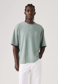 Παντελόνι με κοντά μανίκια υπερμεγέθους από απαλό βαμβάκι σε απόχρωση μέντας. Διαθέτει μικρό γραφικό στο αριστερό στήθος και άνετη εφαρμογή. Συνδυάζεται με λευκό παντελόνι.