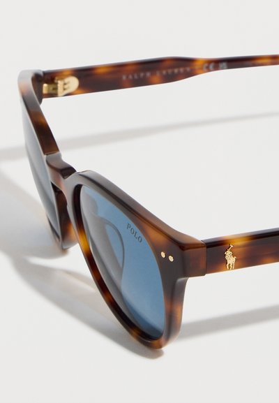 Solbriller med firkantet ramme i skilpaddehud, blå linser, liten gulllogo av en polo-spiller på stangen, og "POLO"-tekst på linsen.