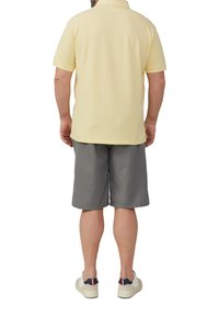 Hellgelbes Polo-Shirt, graue Shorts und weiße Turnschuhe. Das Shirt hat einen klassischen Kragen, kurze Ärmel und einen lässigen Schnitt.