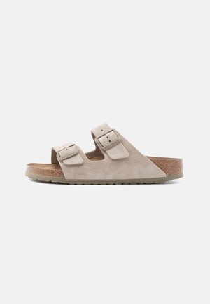 Béžová semišová sandála Birkenstock s dvoma nastaviteľnými remienkami a korkovou stielkou na jednoduchom bielom pozadí.