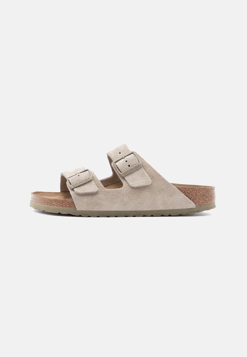 Μπεζ σουέντ σανδάλι Birkenstock με δύο ρυθμιζόμενους ιμάντες και φελλό πάτο σε απλό λευκό φόντο.
