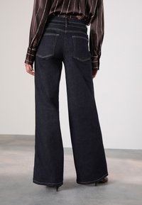 Jeans bleu marine à jambes larges et taille haute, avec deux poches arrière et des détails de coutures visibles. Texture en denim lisse.