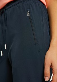 Marineblauwe lichte broek met een elastische tailleband, een ritssluitingzak en een trekkoord. Voorzien van een klein geborduurd logo aan de zijkant.