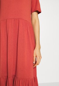 Rotes Baumwollkleid mit kurzen Ärmeln, Rundhalsausschnitt und gerafftem, gestuftem Rock. Weiche Textur mit sichtbaren Nähten und ausgestellter Silhouette.