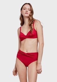 Crveni bikini set s prevrnutim bandeau topom i visokim donjim dijelom s detaljem čvora. Glatka, rastezljiva tkanina, minimalistički dizajn.